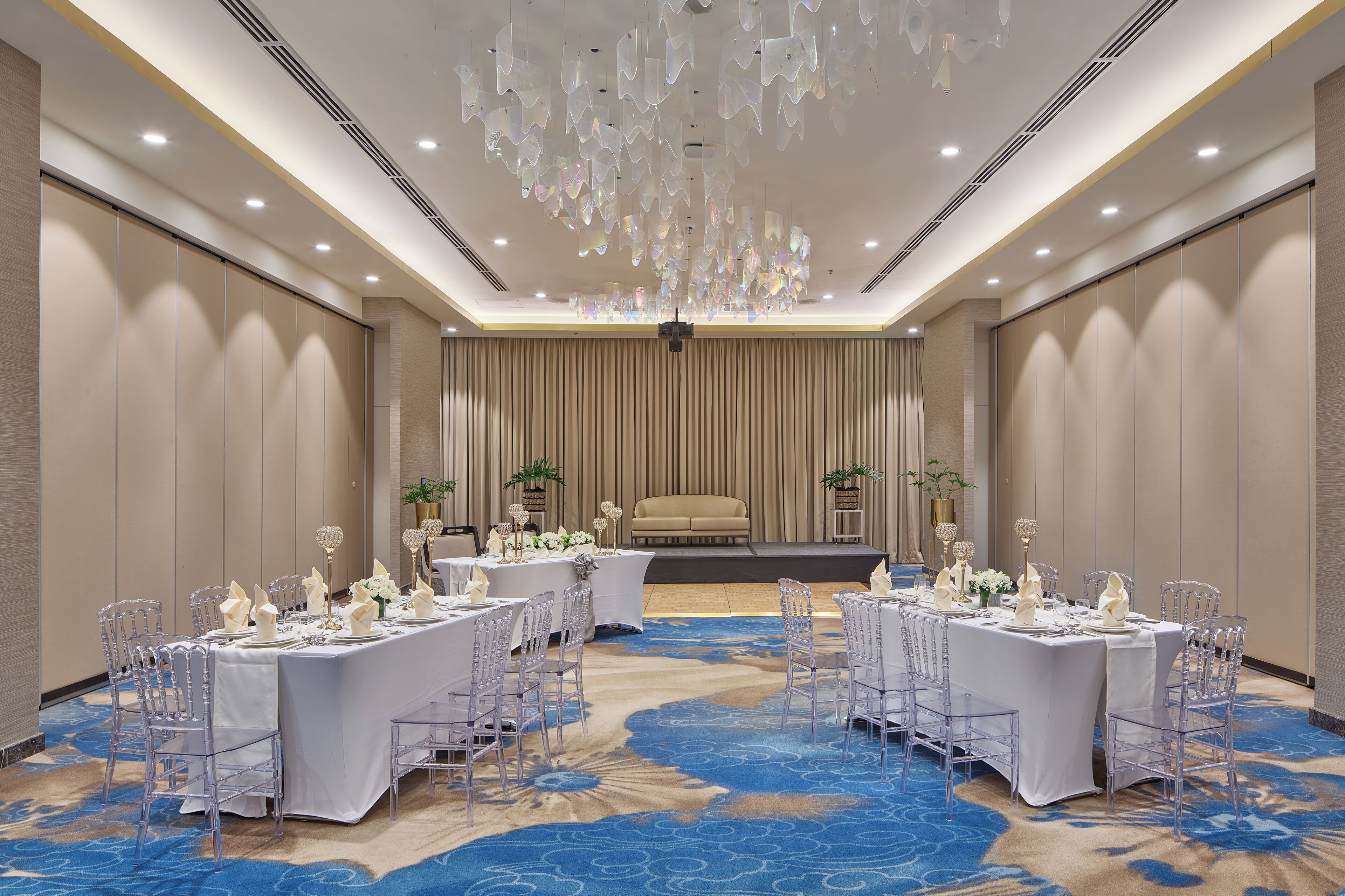 A conference room with a stage, round tables with chairs, and a patterned carpet.