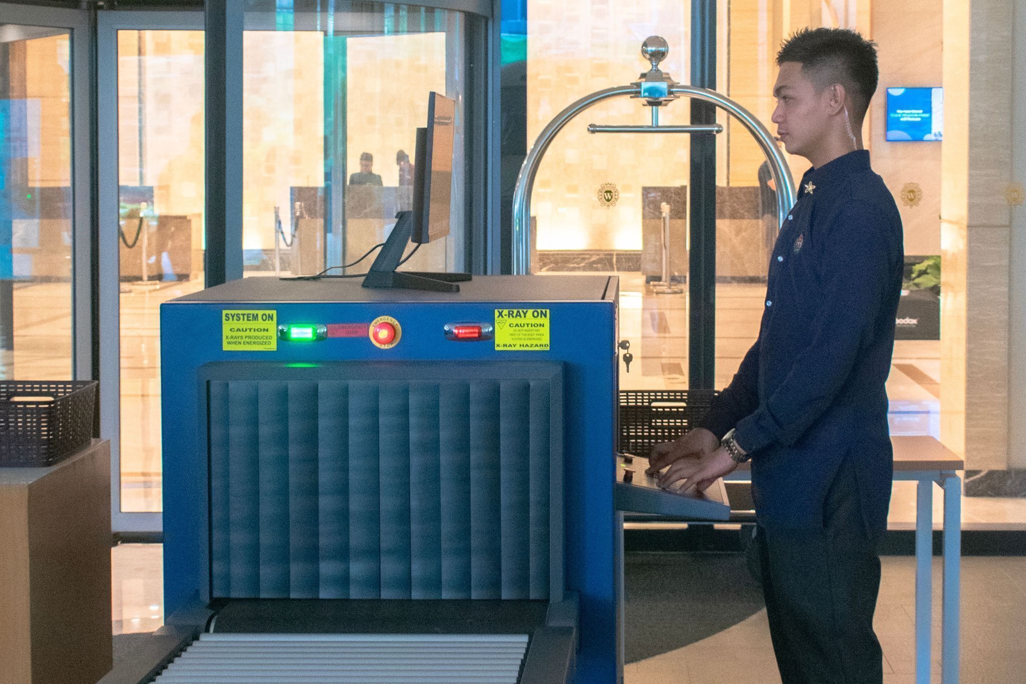A man standing in front of a blue security checkpoint with a metal detector and a sign indicating the system is on.