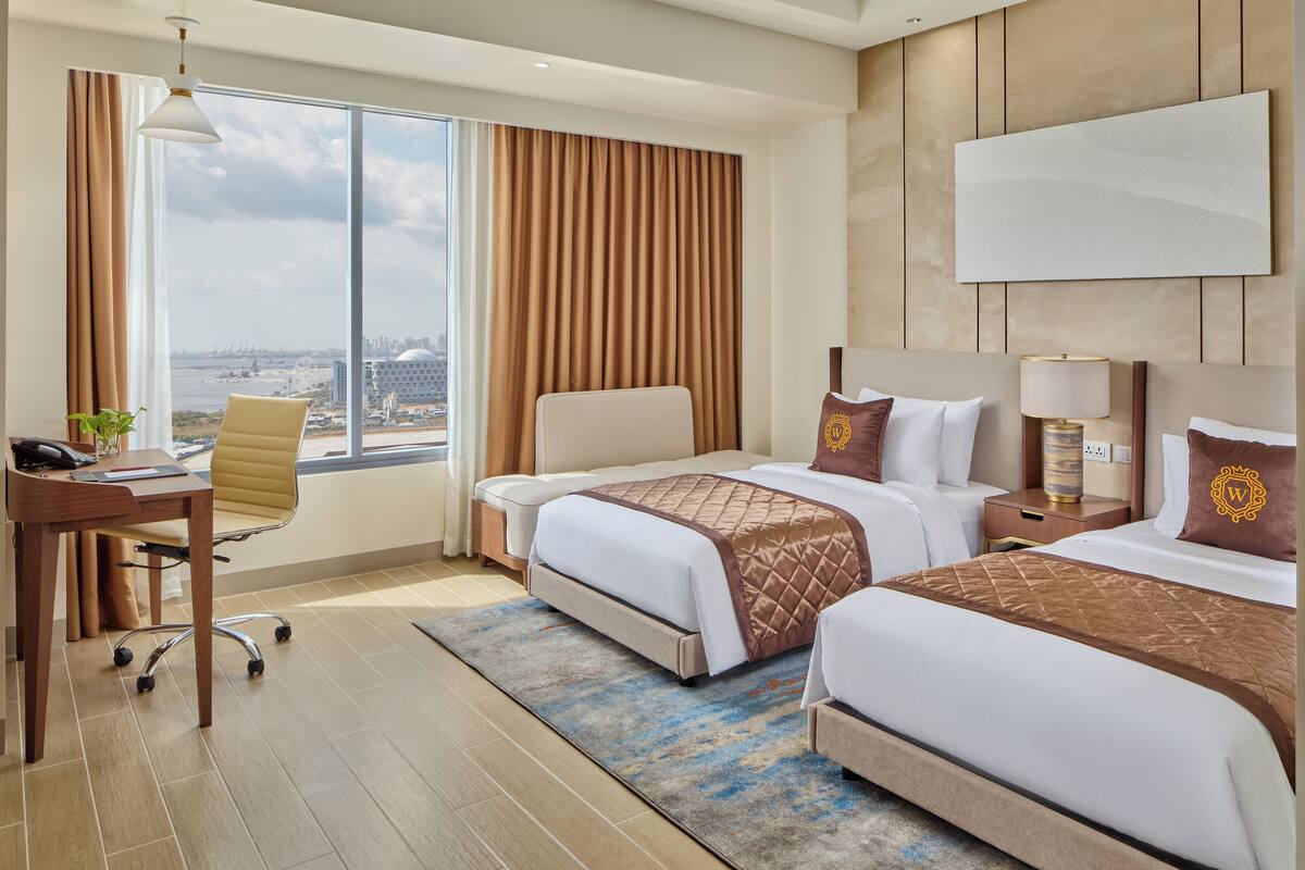 A hotel room with two beds, a desk, and a view of the city.