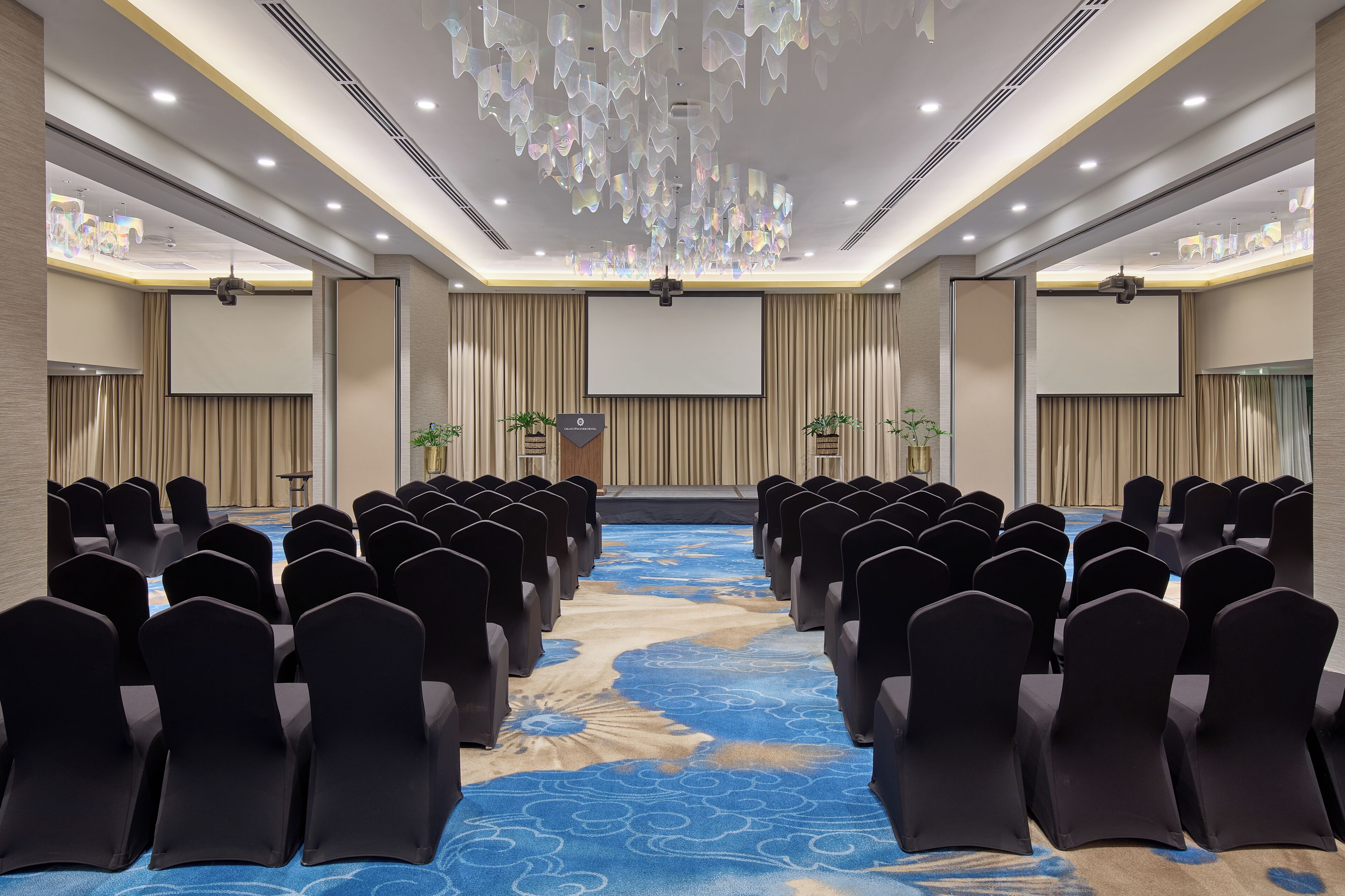 A conference room with rows of chairs, a stage, and a blue carpet with a floral pattern.