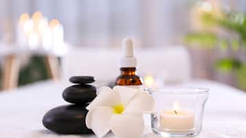 A spa setting with a white flower, a dropper bottle, and a lit candle on a white surface.