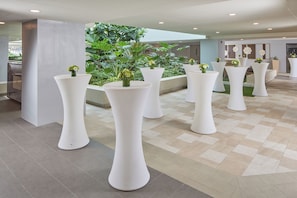 A spacious indoor area with white pedestal tables, some with small plants, and a checkered floor.