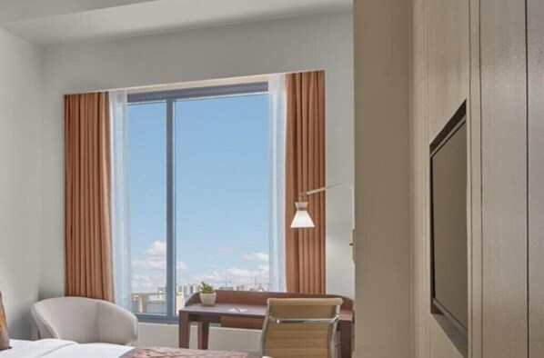 Una habitación de hotel con un ventanal grande, una cama, un escritorio con una silla y un televisor.