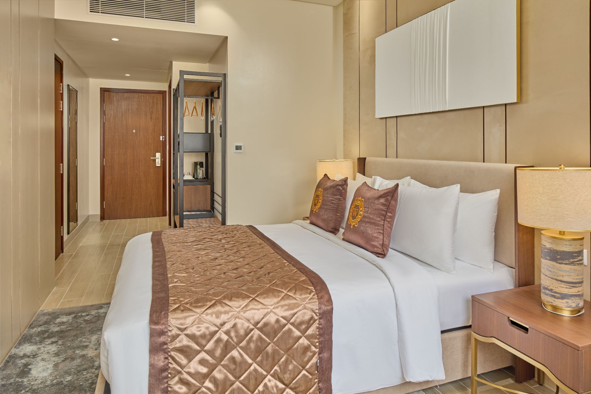 Habitación de hotel con una cama grande, una mesita de noche con lámpara, un armario y un espejo en la pared.