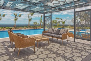 A poolside area with wicker furniture, a sofa, and a view of the ocean. - Grand Westside Manila Bay (Parañaque)