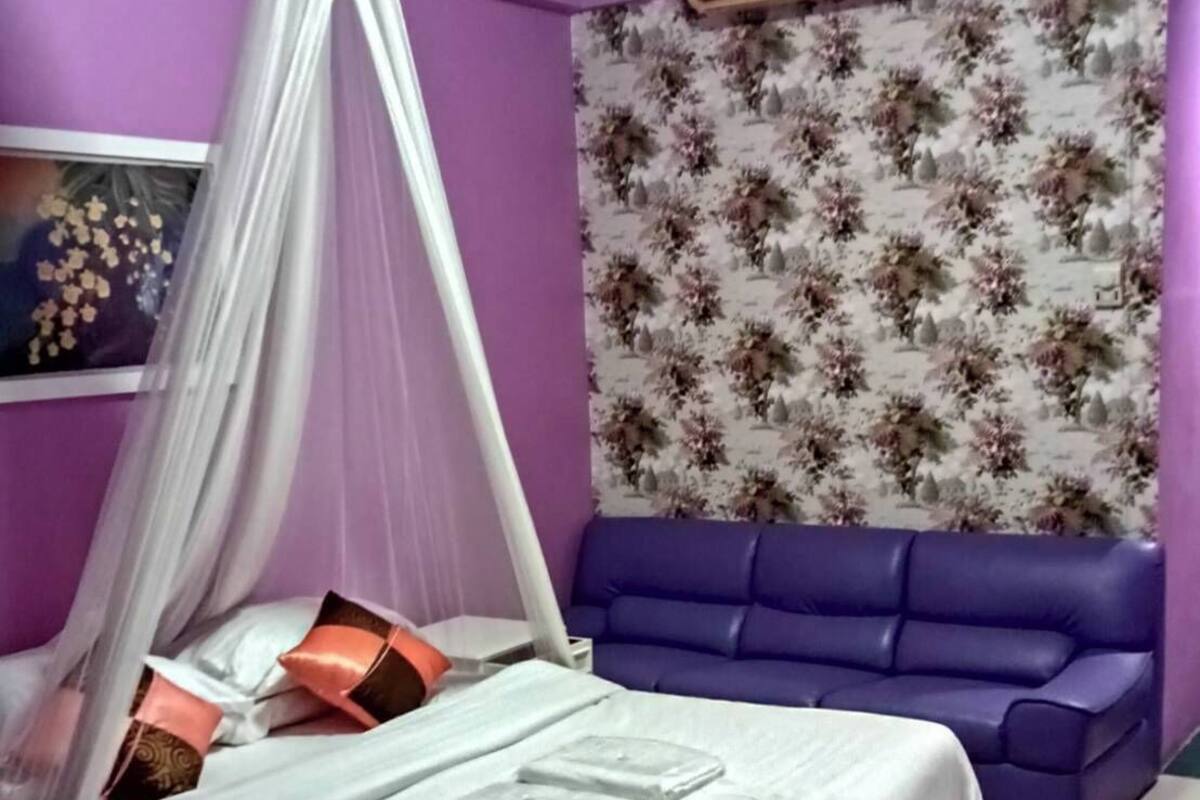 A bedroom with a bed, a blue sofa, and a floral wallpaper.
