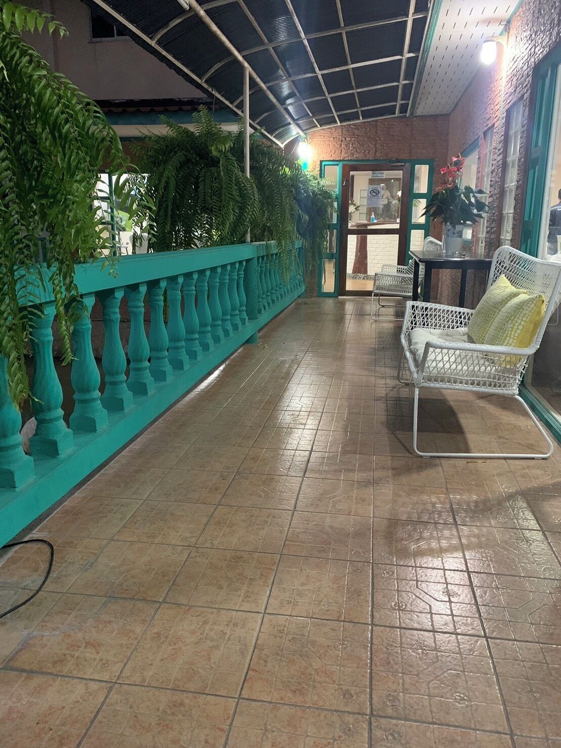 A corridor with a tiled floor, a teal railing, and a white chair with a yellow cushion.