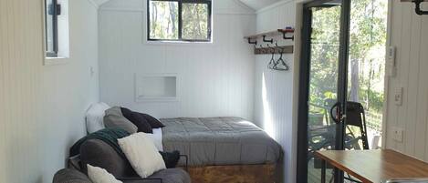 A compact bedroom with a bed, a chair, a table, and a window.