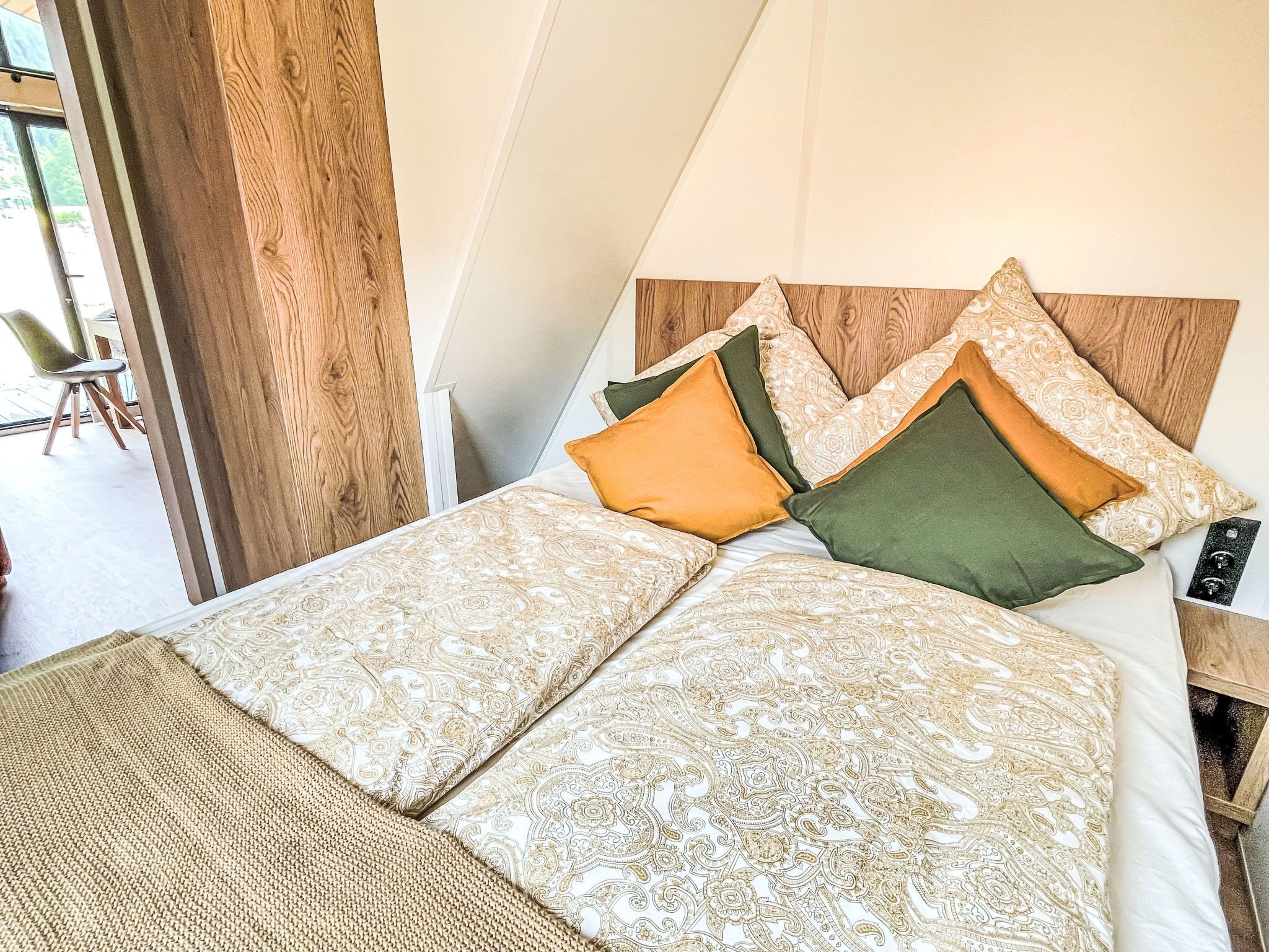 A bed with patterned bedding and pillows, a wooden headboard, and a view of an outdoor area.