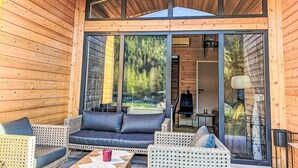 Une cabane en bois avec une porte en verre donnant sur un patio aménagé avec du mobilier d’extérieur.