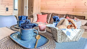Une pièce chaleureuse au décor intérieur en bois, une table à manger dressée avec de la vaisselle en céramique bleue, un verre de jus de fruits, du pain et un panier de viennoiseries.