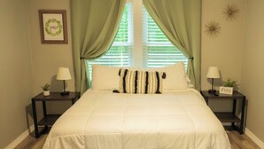A neatly made bed with a white duvet, two bedside tables with lamps, a framed picture on the wall, and a window with green curtains. -  Cozy country home with a beautiful creek at the back of the property.  (Mulberry)