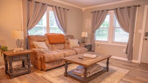A cozy living room with a brown leather sofa, a wooden coffee table, and a patterned rug. -  Cozy country home with a beautiful creek at the back of the property.  (Mulberry)