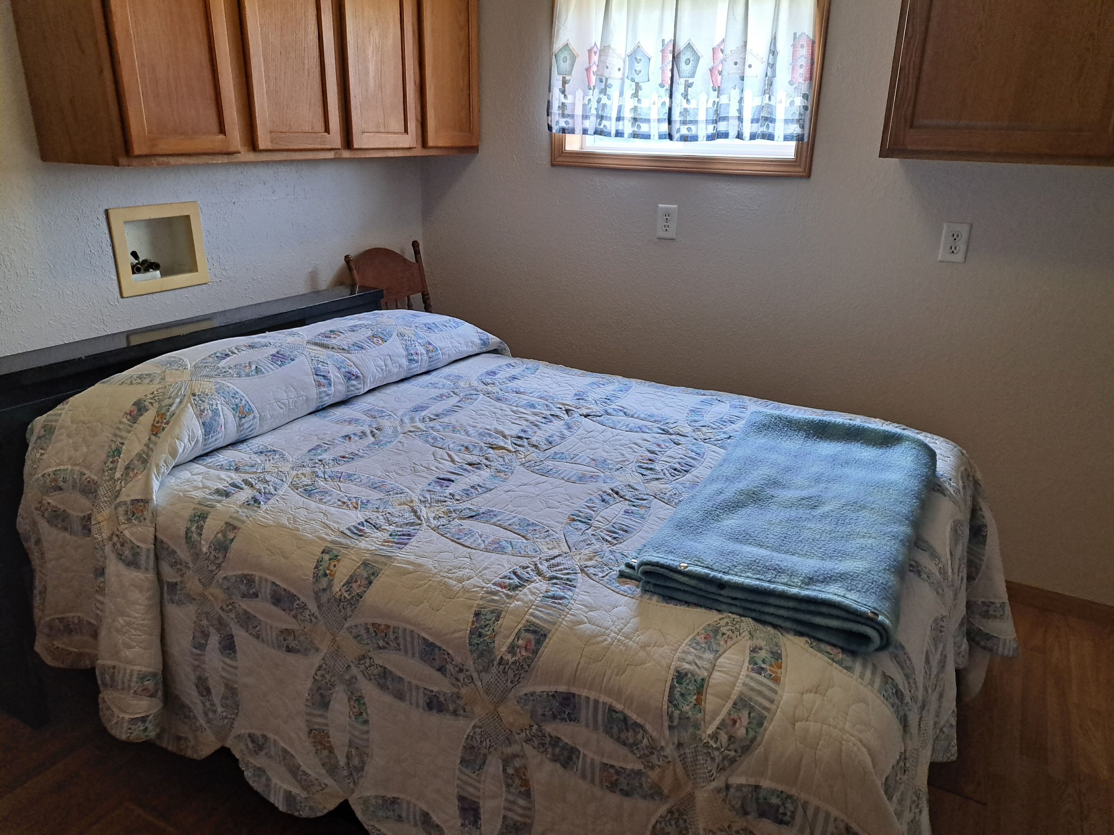 Un dormitorio con una cama, armarios de madera, un ventanal con cortinas y un pequeño estante en la pared.