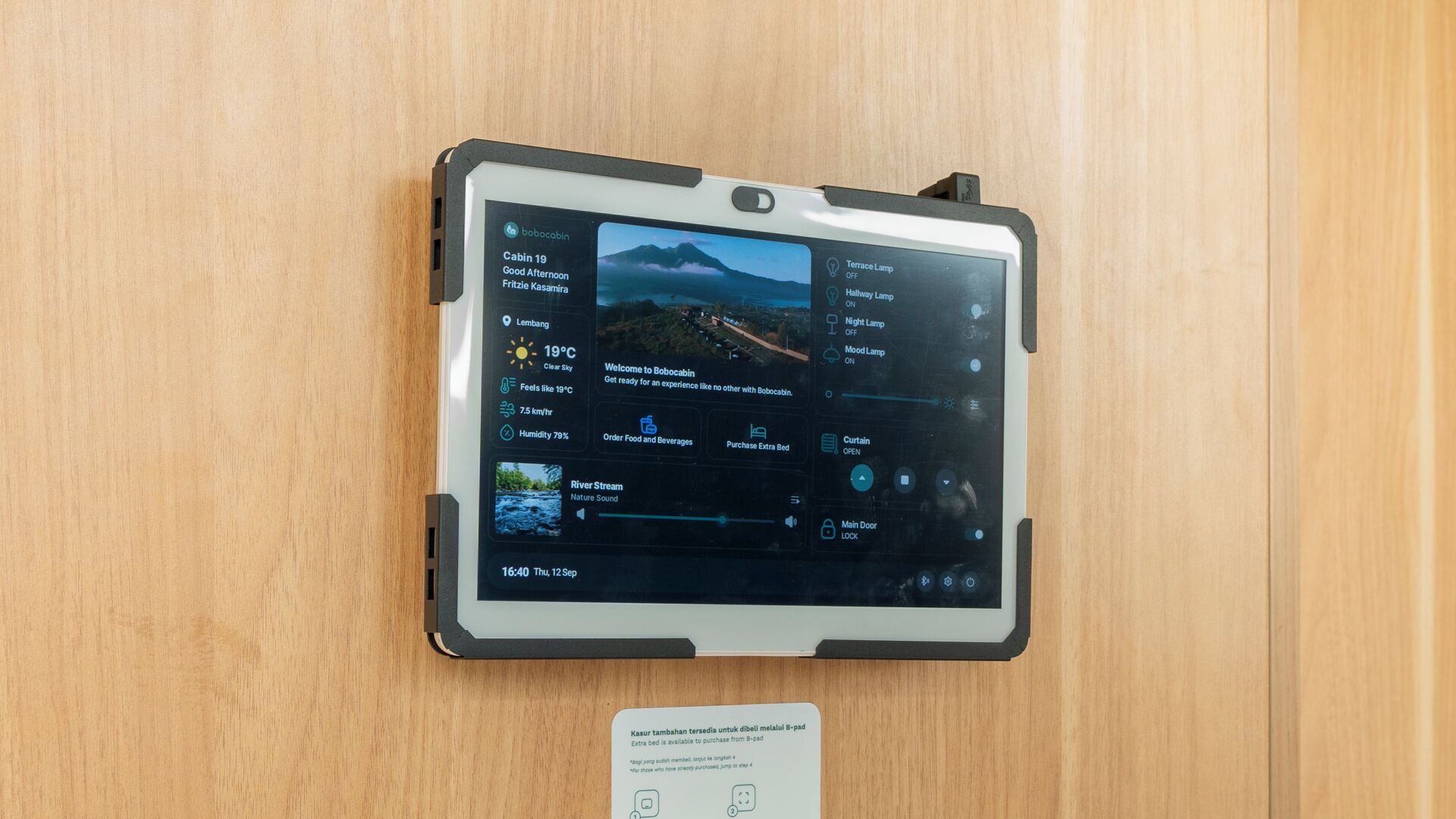 Una tableta muestra los servicios de la habitación, incluyendo vistas a la montaña, información meteorológica y opciones de control para luces y cortinas.