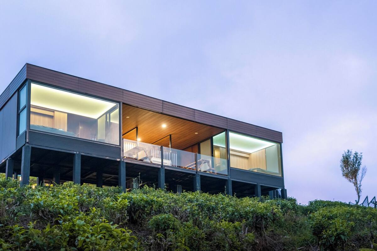 Una casa moderna de dos pisos con amplios ventanales, un balcón y una terraza de madera.