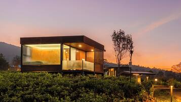 Una casa moderna con un amplio ventanal, un balcón y vistas del paisaje circundante.