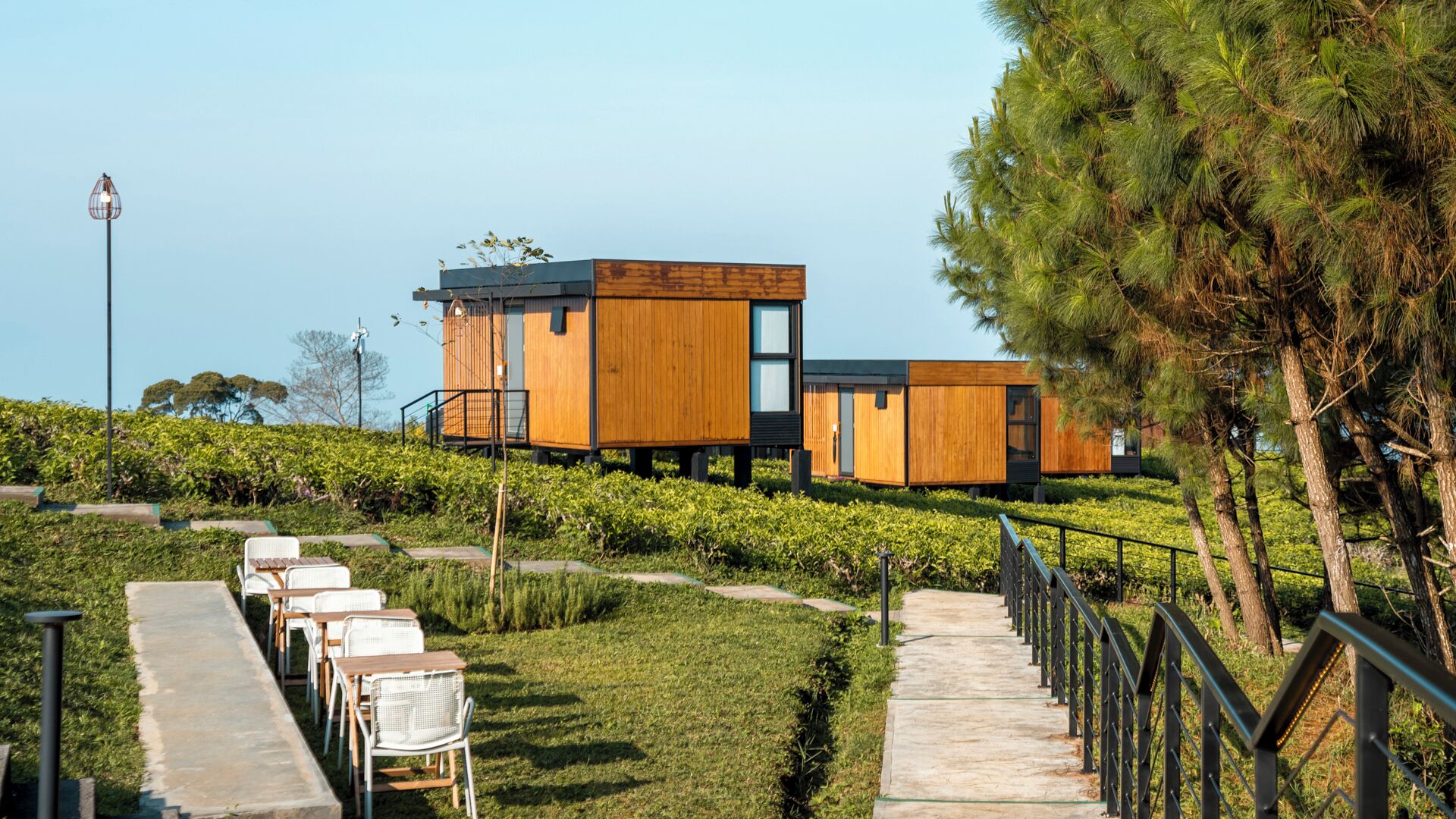 A modern wooden cabin with a glass balcony, surrounded by a well-maintained garden and a paved pathway.