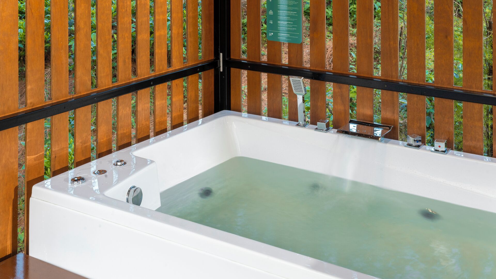 A white bathtub with a single faucet and a control knob, set against a wooden fence with vertical slats.
