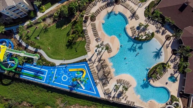An aerial view of a resort with multiple swimming pools, a water slide, and a children's play area.