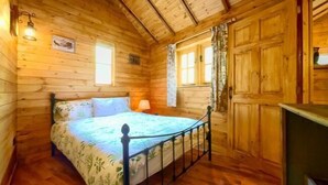 Un dormitorio de cabaña de madera con cama, mesita de noche, lámpara y ventana con cortinas.