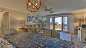 A spacious living area with a large wooden dining table, a ceiling fan, and a balcony with sliding doors. - Aegean 210 (Destin)