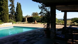 Un área de piscina con un patio de piedra, una zona de estar cubierta y vistas al campo.
