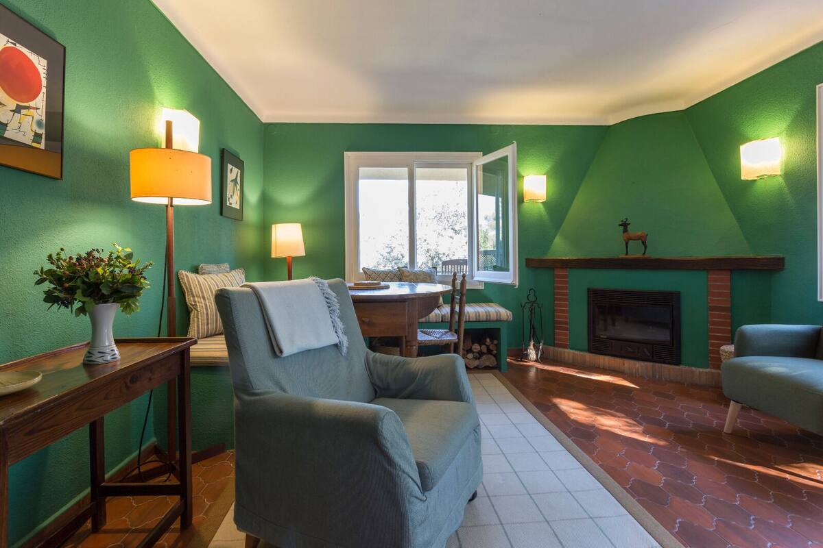 Una sala de estar con paredes verdes, chimenea, mesa de comedor con sillas y sofá.