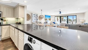 A modern kitchen with a large island, built-in appliances, and a dining area with a view. - Aegean 211 (Destin)