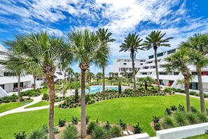 A resort with multiple white buildings, palm trees, a swimming pool, and a well-maintained lawn. - Aegean 211 (Destin)