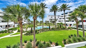 A resort with multiple white buildings, palm trees, a swimming pool, and a well-maintained lawn. - Aegean 211 (Destin)