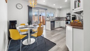 A modern kitchen with white cabinets, a built-in oven, and a coffee machine. There is a dining area with a round table and yellow chairs. - Super Spacious Family Vacation Home! (San Diego)
