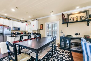 A modern kitchen with white cabinets, a central island, and a dining area with a dark wooden table and chairs.