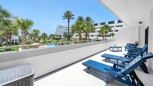 Ein Balkon mit blauen Lounge-Sesseln, einem kleinen Tisch und Blick auf einen Pool.