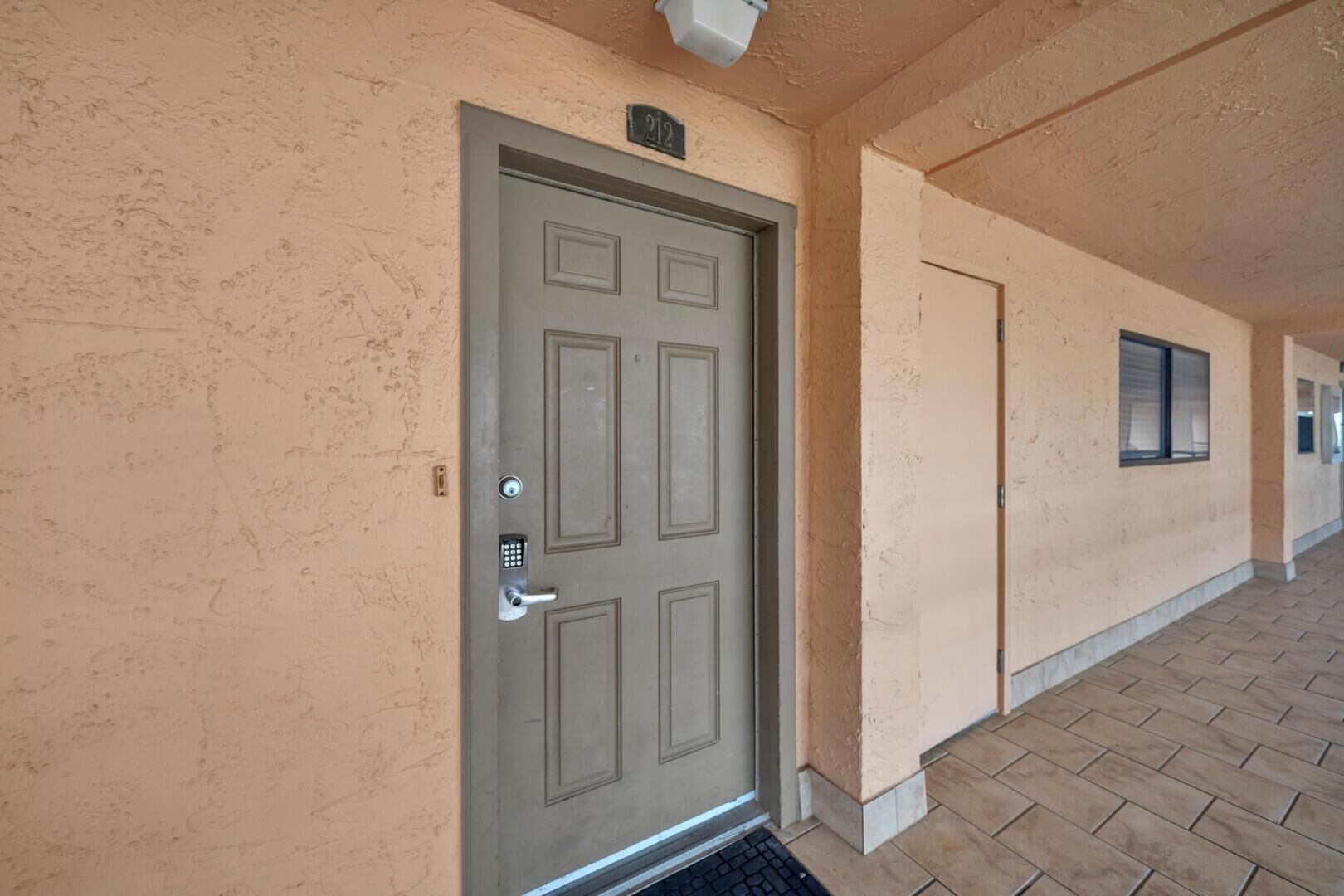 A building entrance with a grey door, a keypad lock, and a small window above the door.