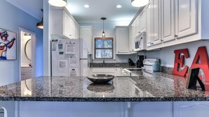 A modern kitchen with white cabinets, granite countertops, and a large island. - Monkey Business (Santa Rosa Beach)