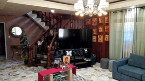 Una sala de estar con una escalera, un televisor, un sofá y una araña.