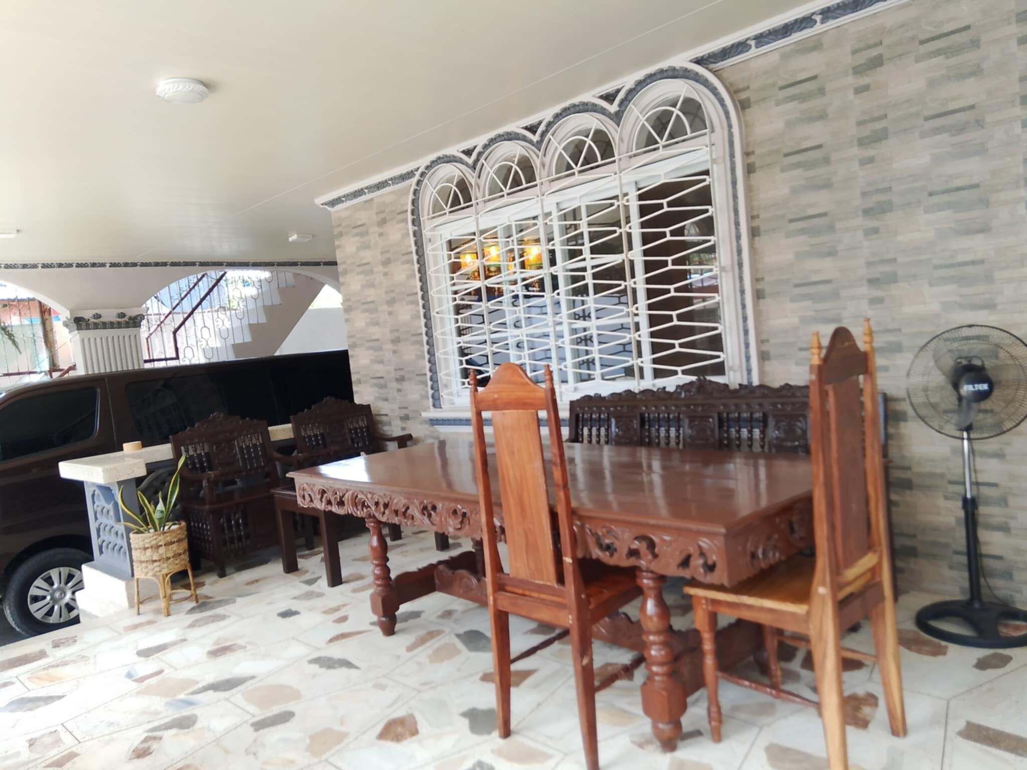 A dining area with a wooden table and chairs, a patterned floor, a decorative window, and a fan.