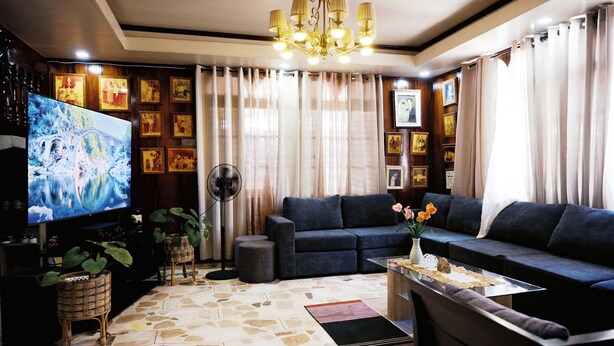 Una sala de estar con un televisor de pantalla plana grande, un sofá de color oscuro, una mesa de centro de vidrio y un tapete estampado.