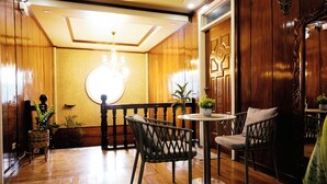 Un hall con suelo de madera, un candelabro, dos sillones y una mesita.