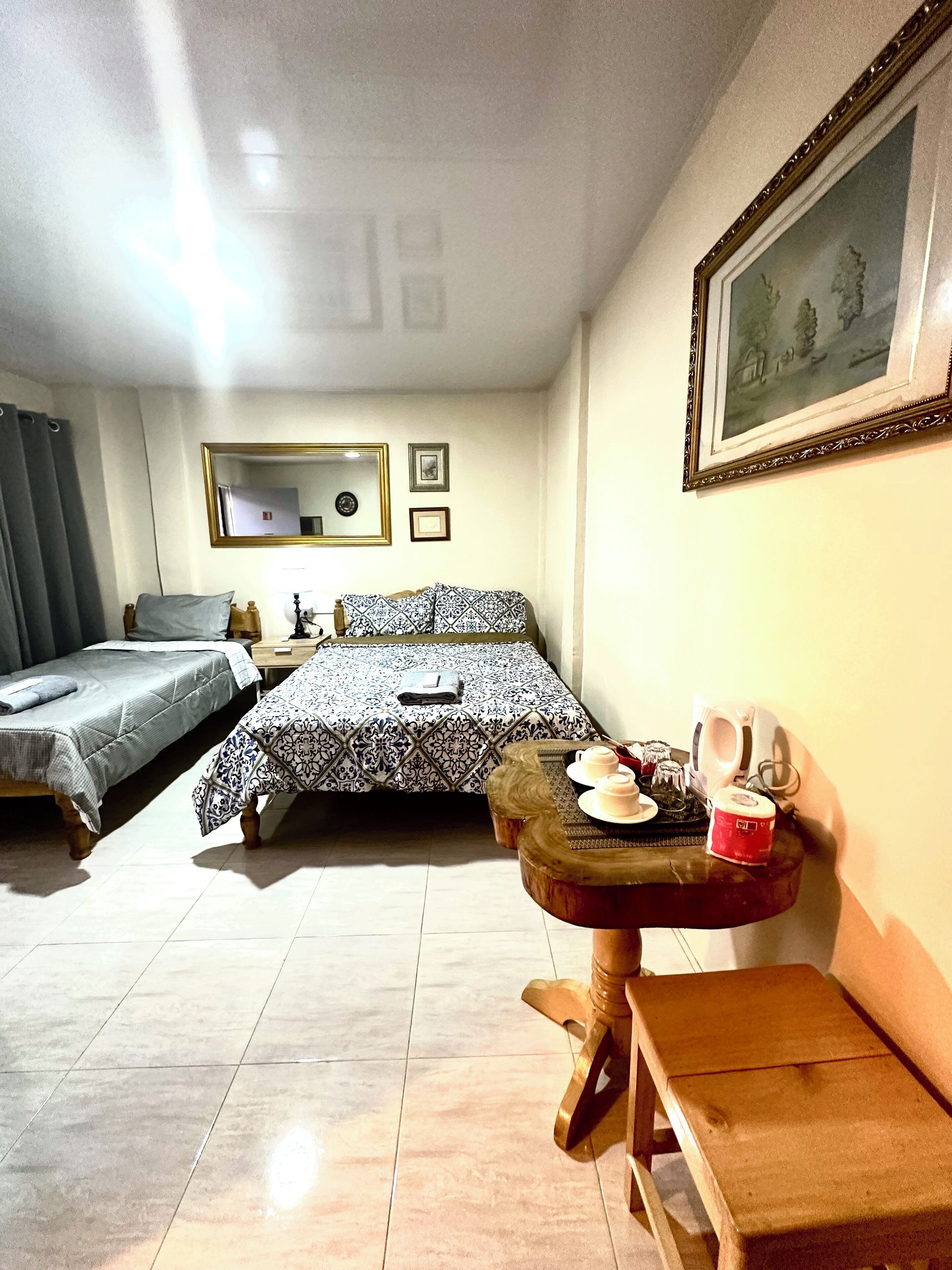 A hotel room with two beds, a small table with a cup and saucer, a mirror, and framed pictures on the wall.