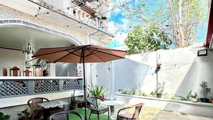 Un patio al aire libre con césped artificial, muebles de mimbre y un paraguas grande.