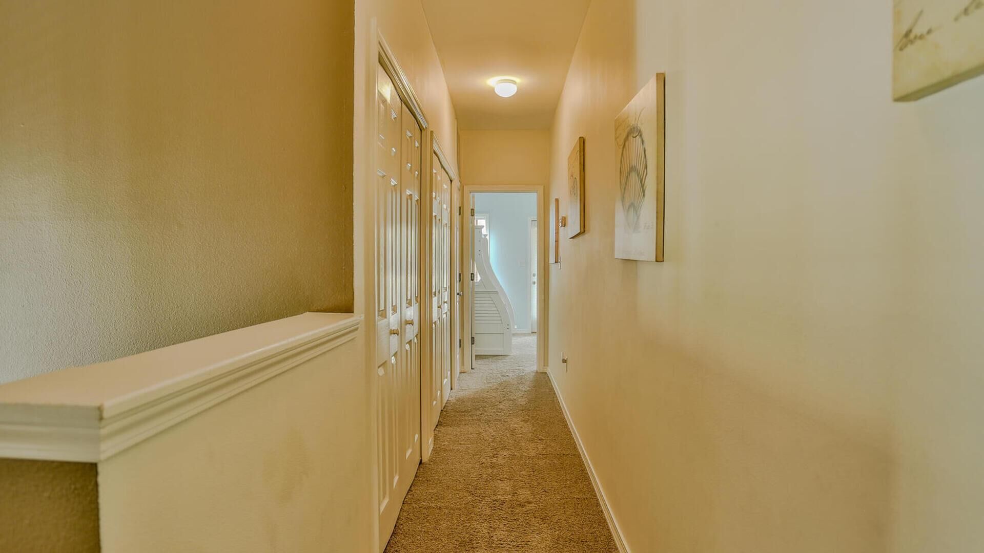 A narrow hallway with a carpeted floor, a white bench on the left, and a staircase at the end.
