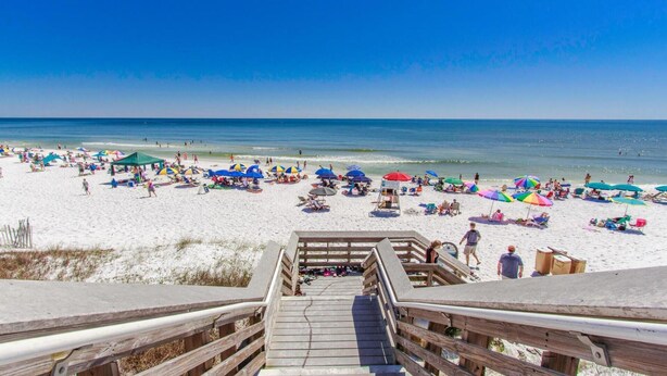 A beach with a wooden staircase leading down to the sand, numerous colorful umbrellas, and people enjoying the beach. - Robbins' Nest (Santa Rosa Beach)