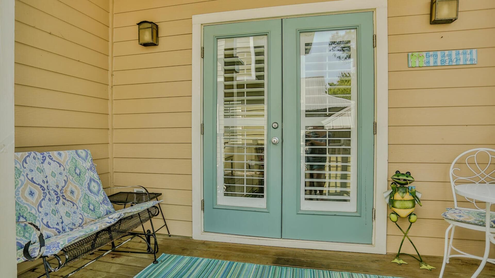Un portico coperto con una porta blu chiaro, una panca decorata con motivi, un tavolino e una scultura a forma di rana ornamentale.