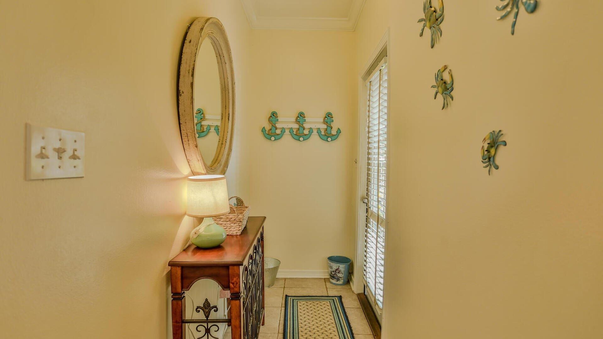 A hallway with a wooden floor, a mirror, a lamp, a small table, a trash can, and wall decorations.