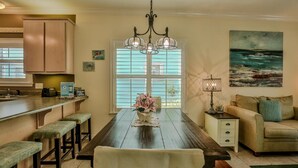 A dining area with a wooden table, benches, a chandelier, and a view of the ocean through large windows. - Robbins' Nest (Santa Rosa Beach)
