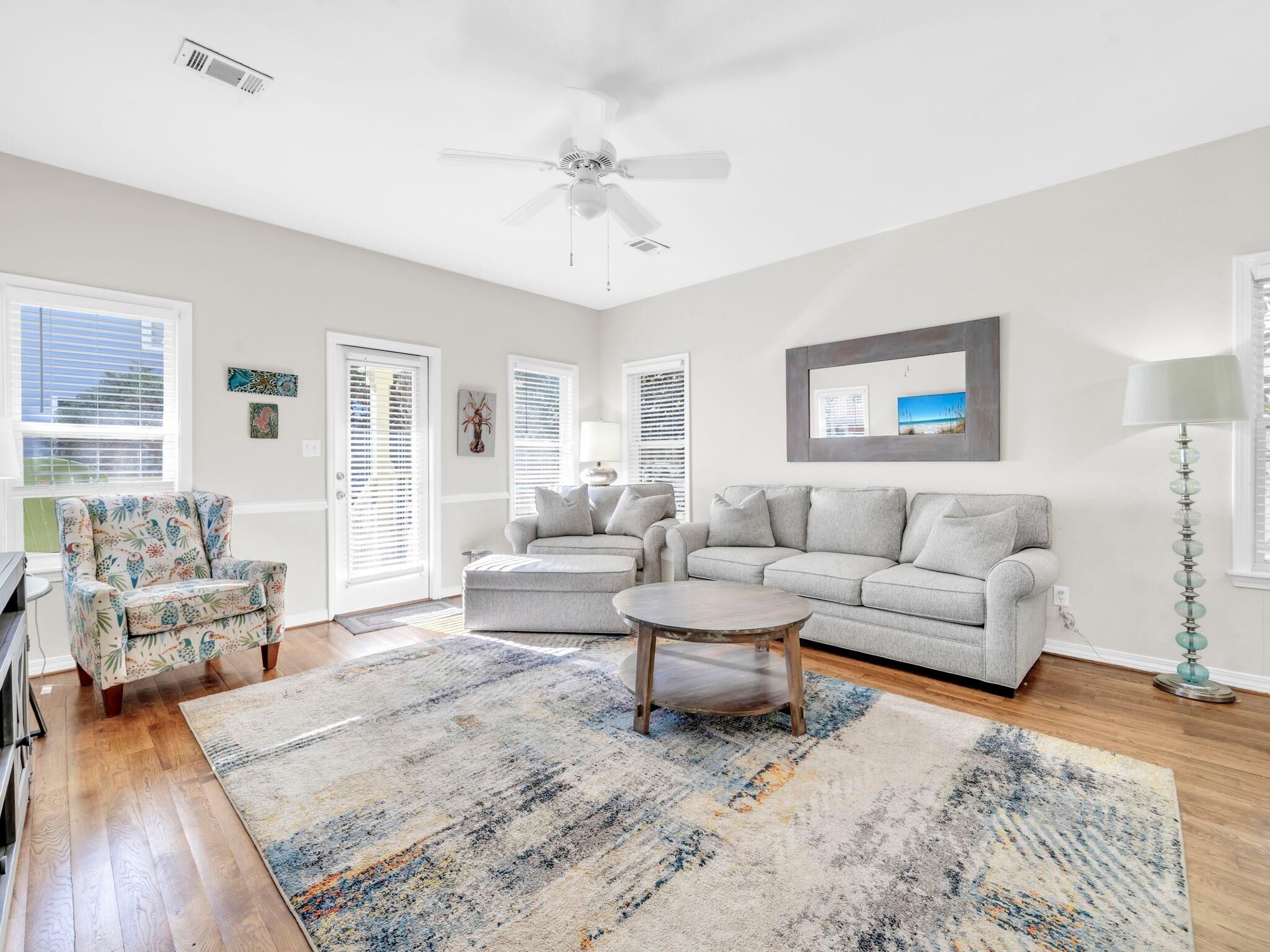 A spacious living room with a grey sofa, a patterned armchair, a coffee table, and a floor lamp.