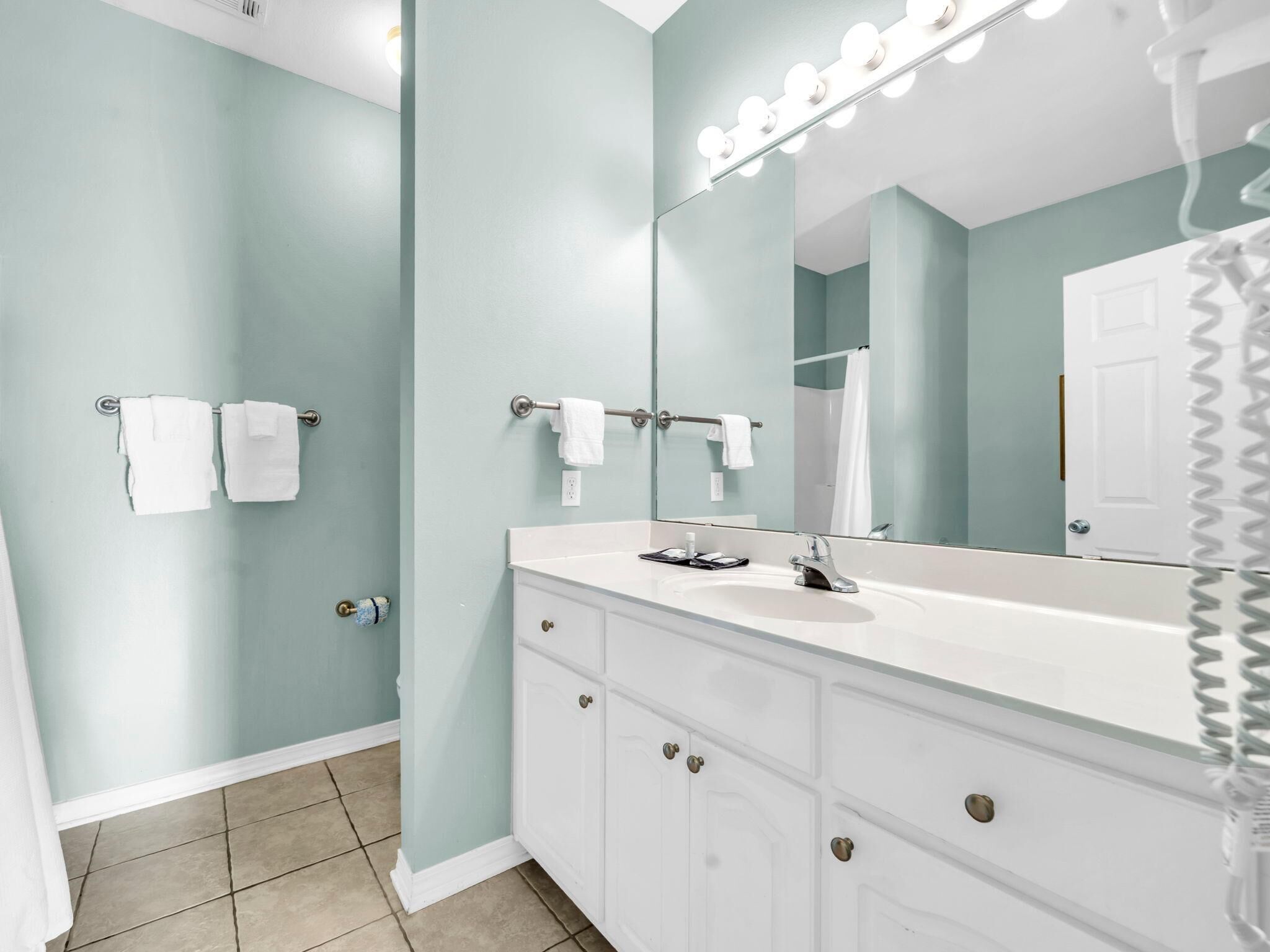 A bathroom with a vanity, a mirror with lights, and a shower curtain.