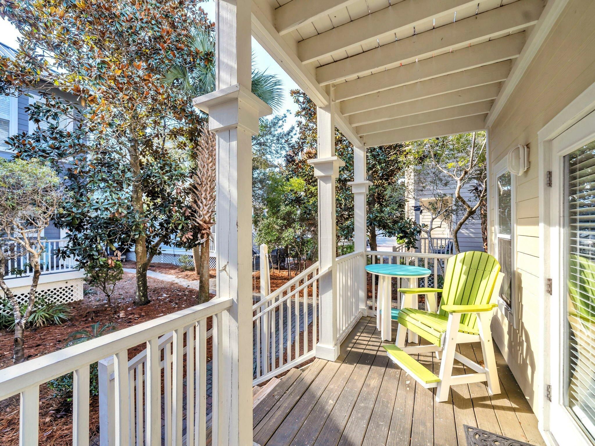 A covered porch with a wooden deck, white railings, and two green Adirondack chairs.